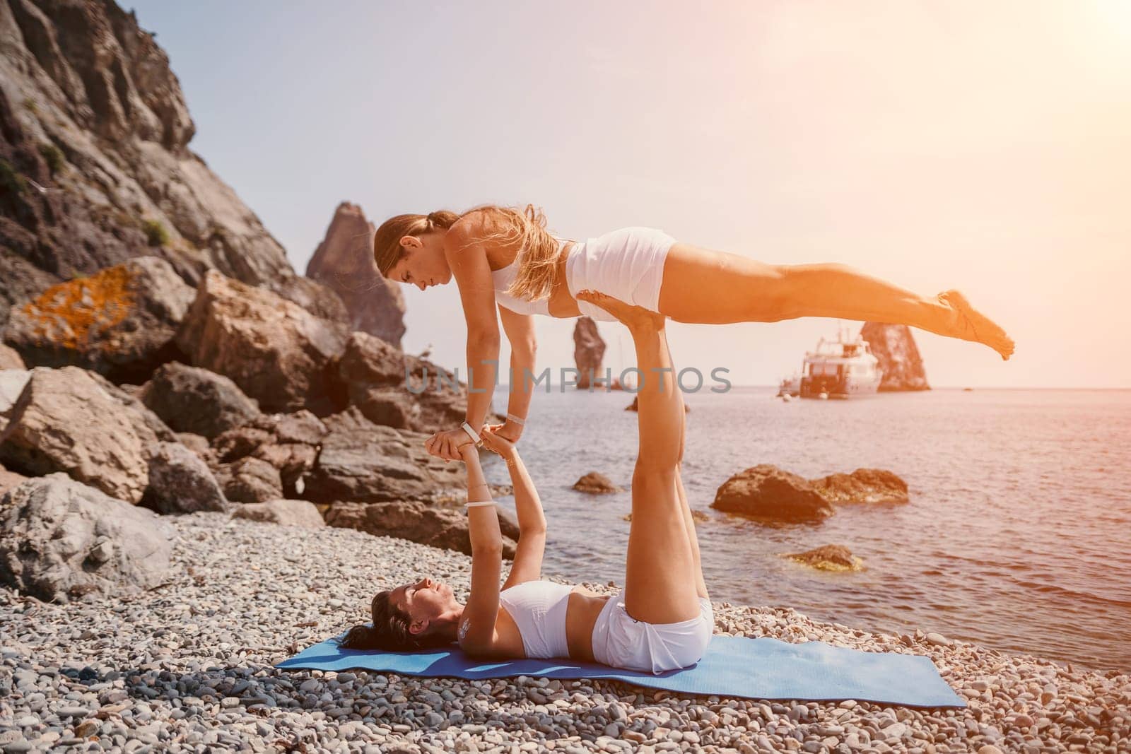 Woman sea yoga. Two happy women practicing yoga on the beach with ocean and rock mountains. Motivation and inspirational fit and exercising. Healthy lifestyle outdoors in nature, fitness concept. by panophotograph