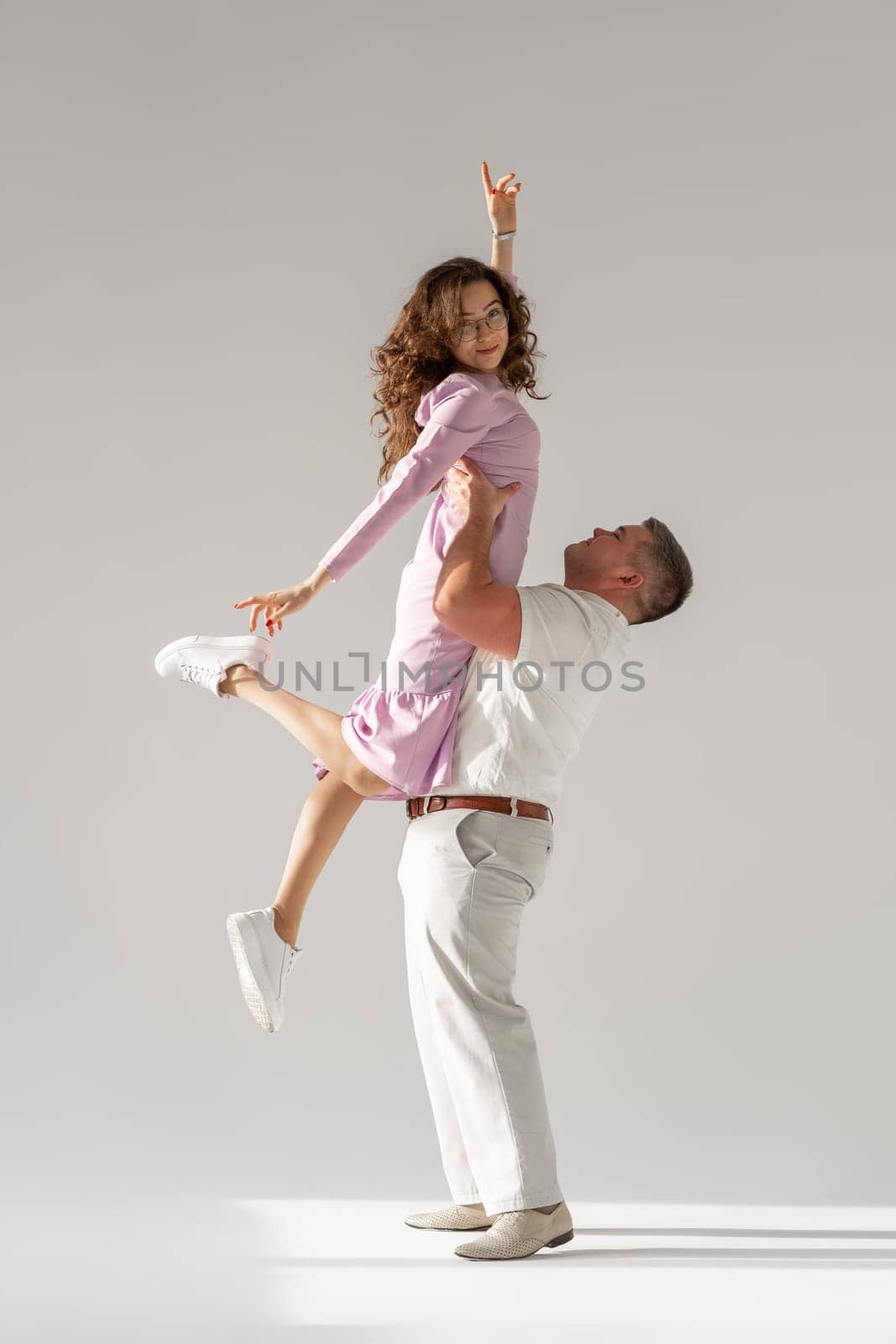 Beautiful young couple dancing on light background. Full length of young beautiful couple bonding while standing against white background