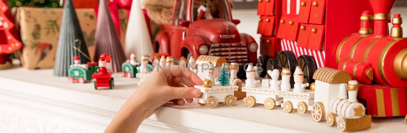 Hands of a child holding a gift, A wooden train toy is carrying New Year's gifts. On a cozy knitted gray sweater. top view.