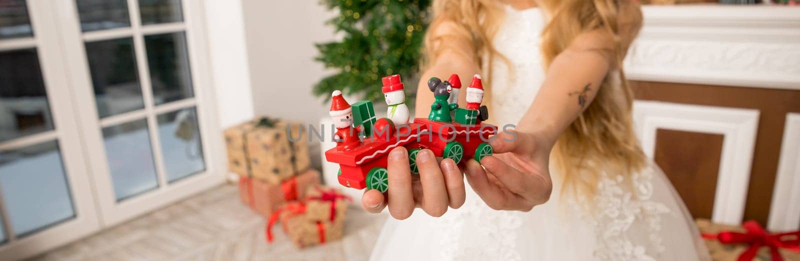 Hands of a child holding a gift, A wooden train toy is carrying New Year's gifts. On a cozy knitted gray sweater. top view.