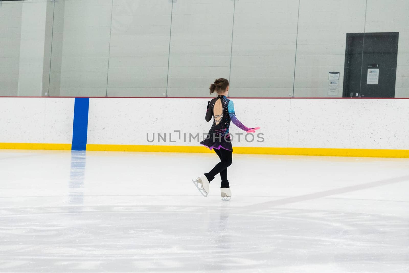 Young girl perfecting her figure skating routine while wearing her competition dress at an indoor ice rink.