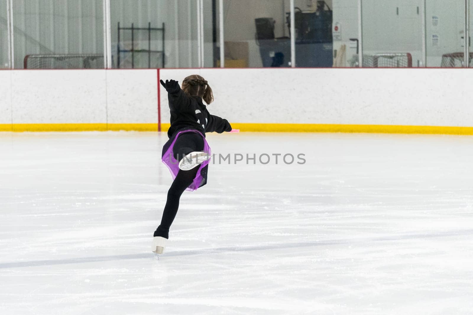 Young girl perfecting her figure skating routine while wearing her competition dress at an indoor ice rink.