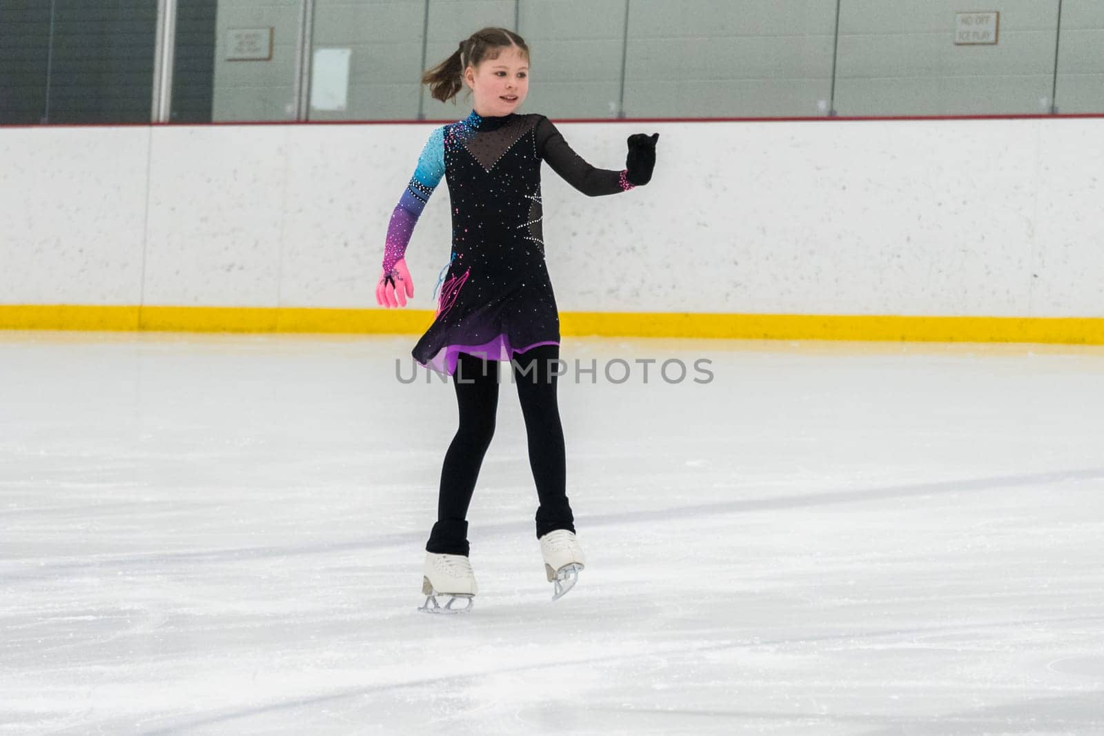 Young girl perfecting her figure skating routine while wearing her competition dress at an indoor ice rink.