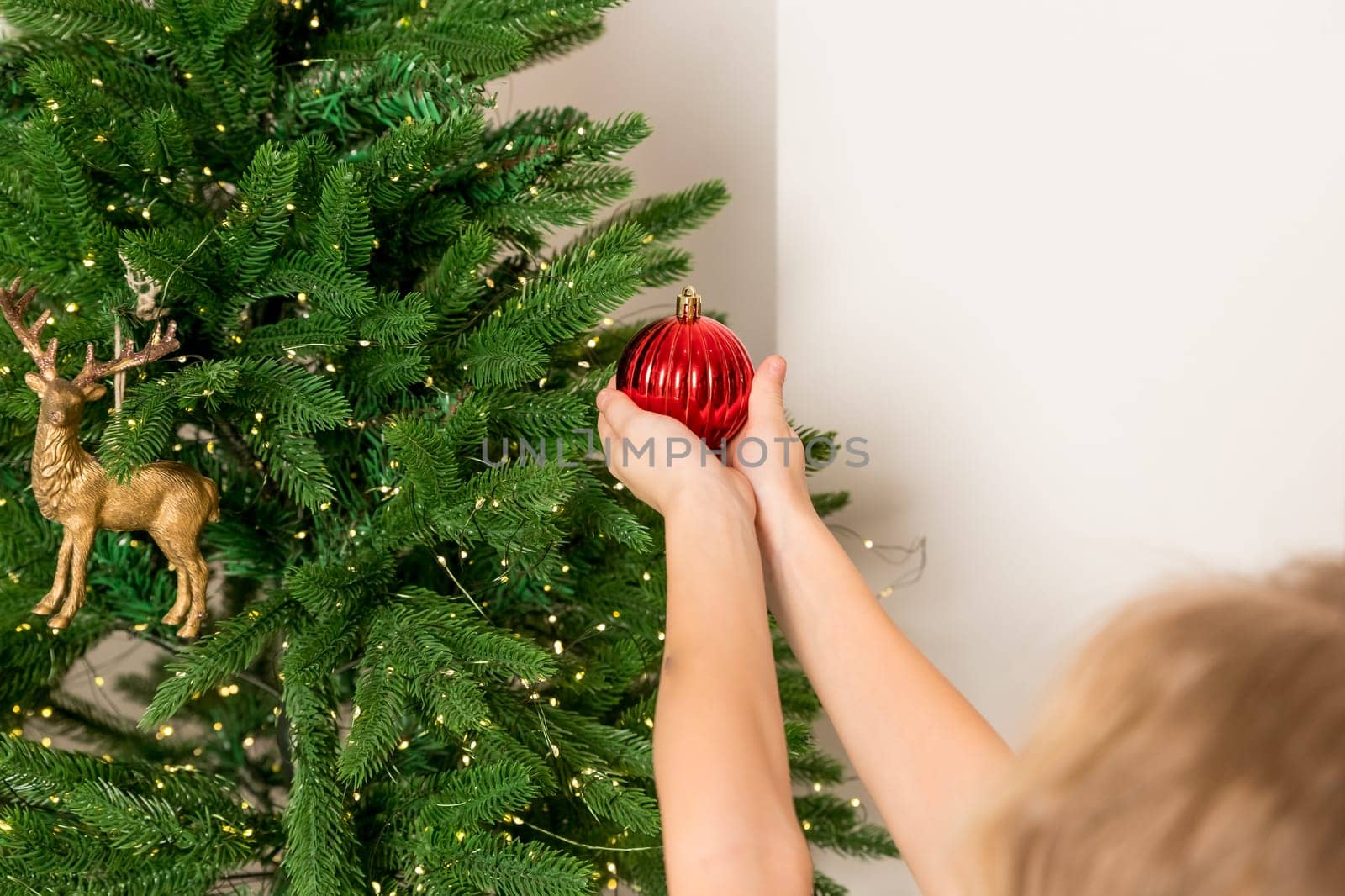 winter holidays and people concept - close up of child hand decorating tree with red ball.Anonymous little girl decorates christmas tree.Cozy magical atmosphere in the room. copy space by YuliaYaspe1979