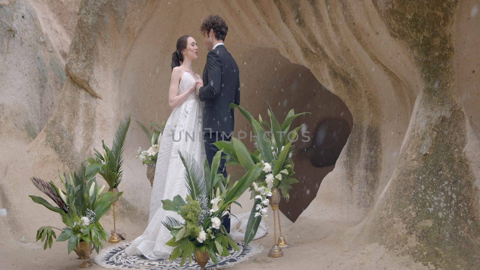 Beautiful newlyweds on rock background. Action. Hugging newlyweds on background of cave during snow. Wedding ceremony at rocks during snowfall.