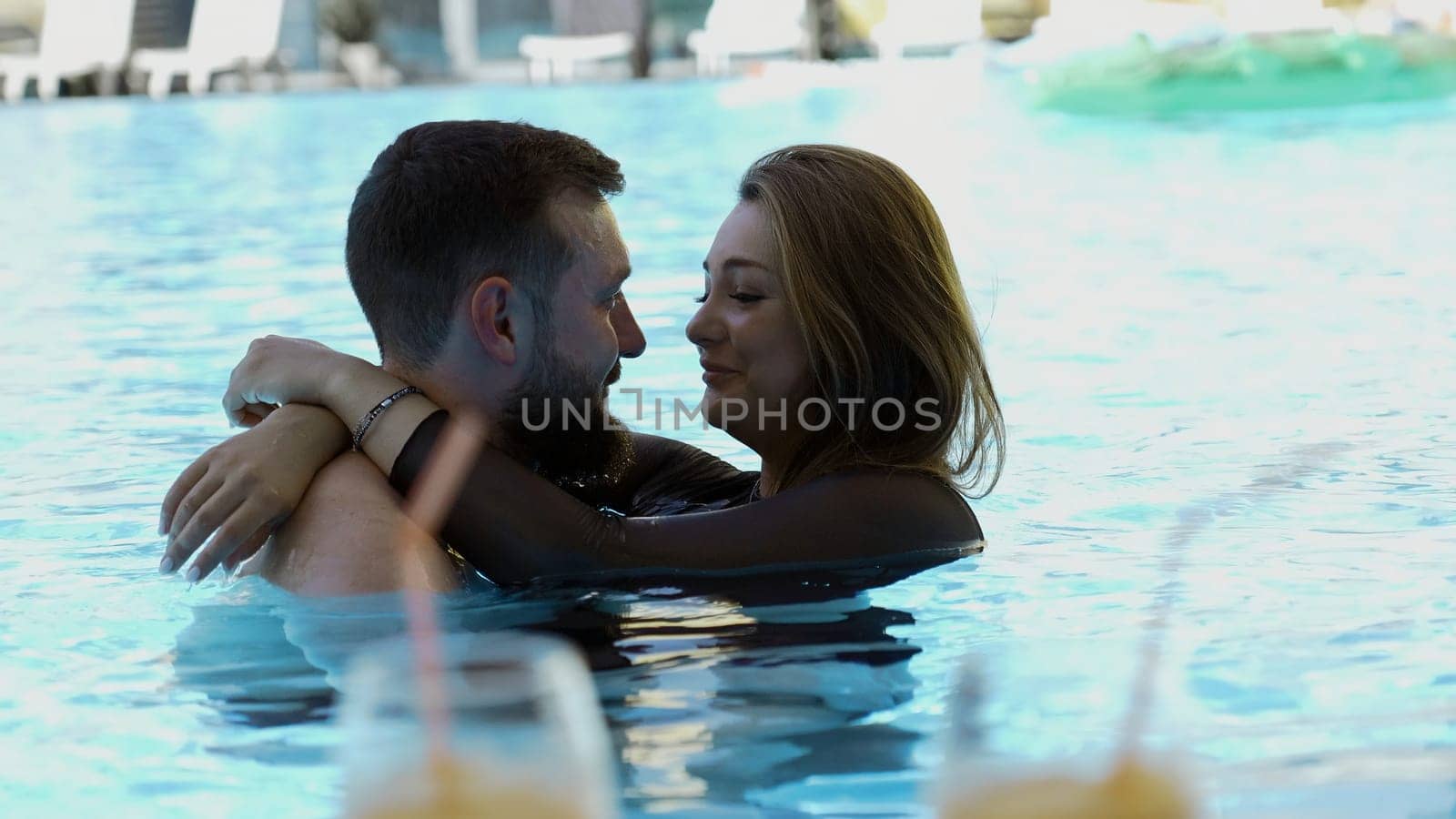 Happy couple embracing in outdoors swimming pool. Clip. Man and woman on a vacation. by Mediawhalestock