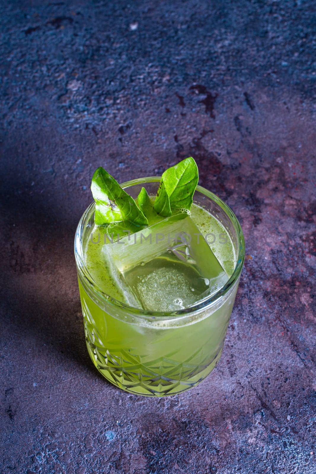 top view of a green cocktail in a glass with ice and a mint leaf on a textured background.