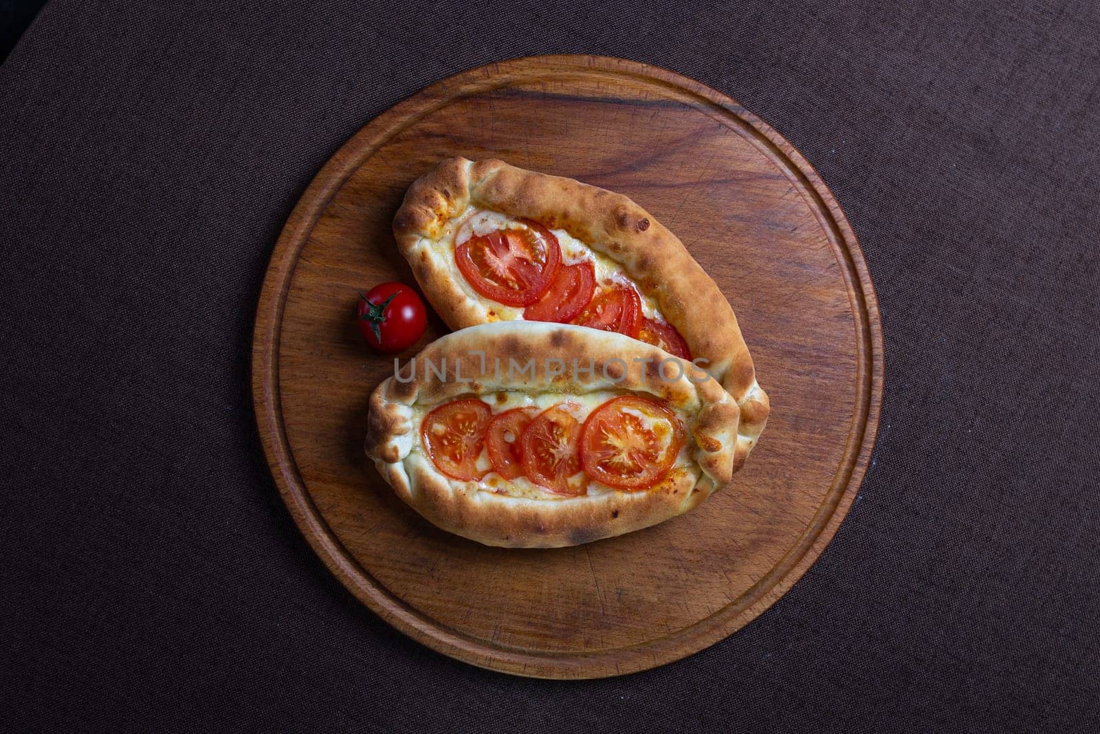 top view of Adjarian khachapuri with tomatoes on a wooden stand by Pukhovskiy