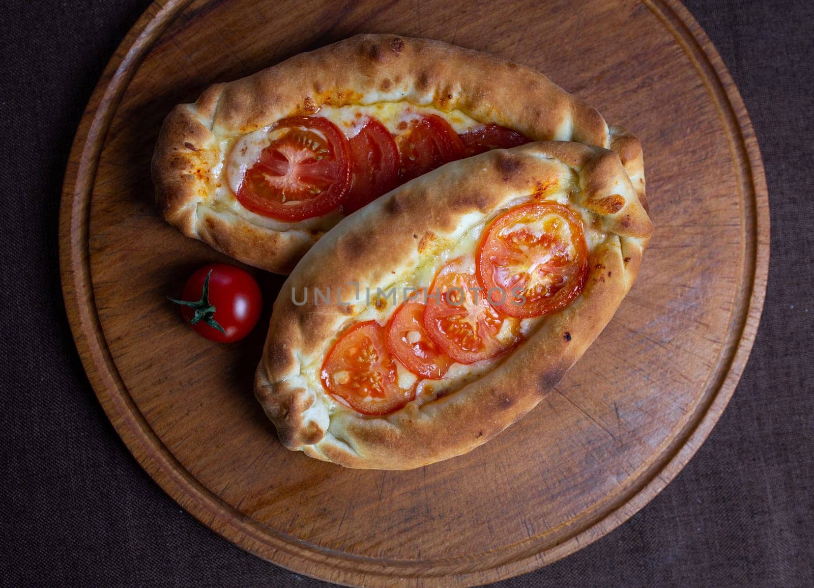 top view of Adjarian khachapuri with tomatoes on a wooden stand by Pukhovskiy