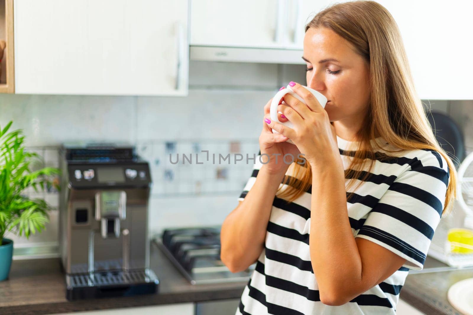 Attractive woman enjoying freshly made coffee in the kitchen in the morning.