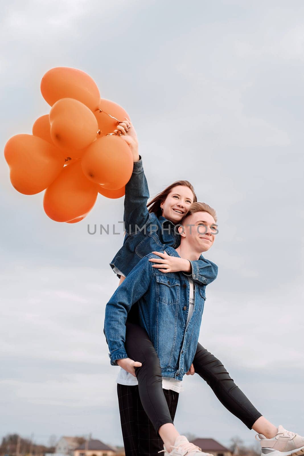 Color of the year 2024: Peach Fuzz. Valentines Day. Young loving couple hugging and holding heart shaped balloons outdoors