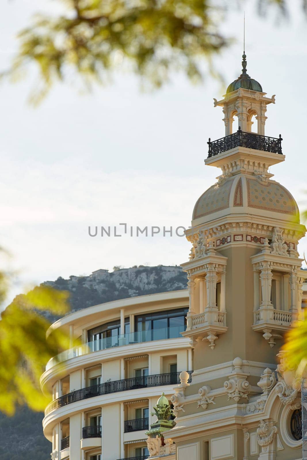 Monaco, Monte-Carlo, 21 October 2022: Towers of Casino Monte-Carlo at sunset, the famous hotel de Paris and mountain are on background, wealth life, famous landmark, pine trees, blue sky. High quality photo