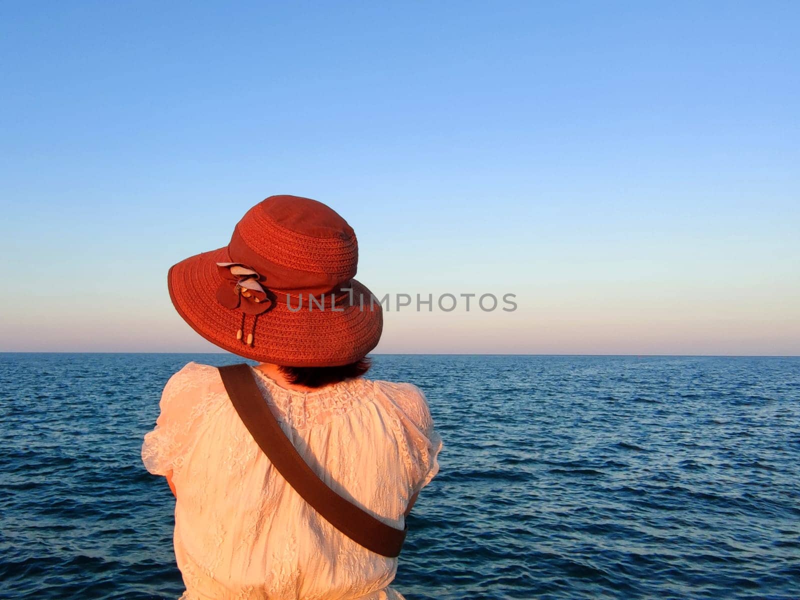 girl in a hat against the backdrop of the sunset sea horizon, rear view.