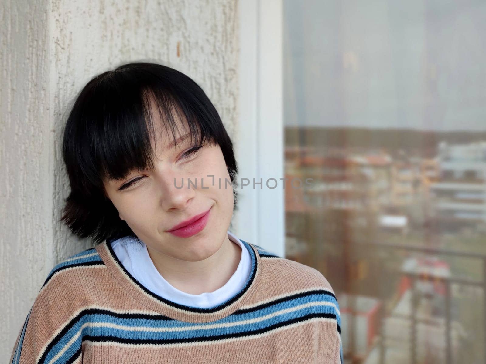 portrait of a smiling brunette teenage girl against the background of a window.