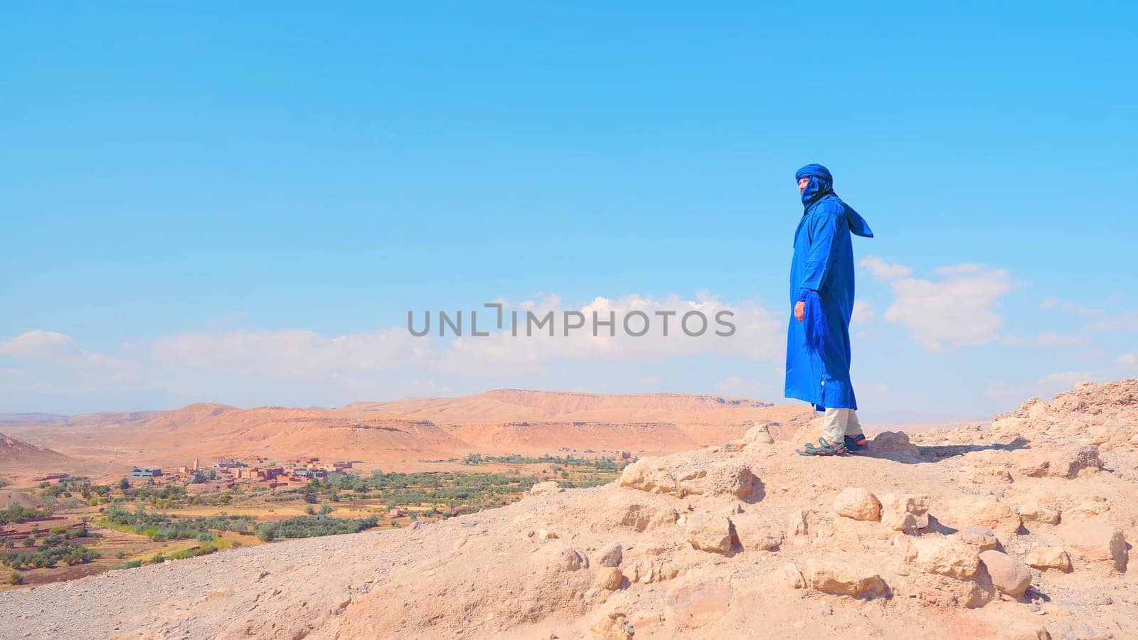 Man on background of oasis. Action. Man in Arab suit stands over oasis in desert. Beautiful man in desert on background of oasis.