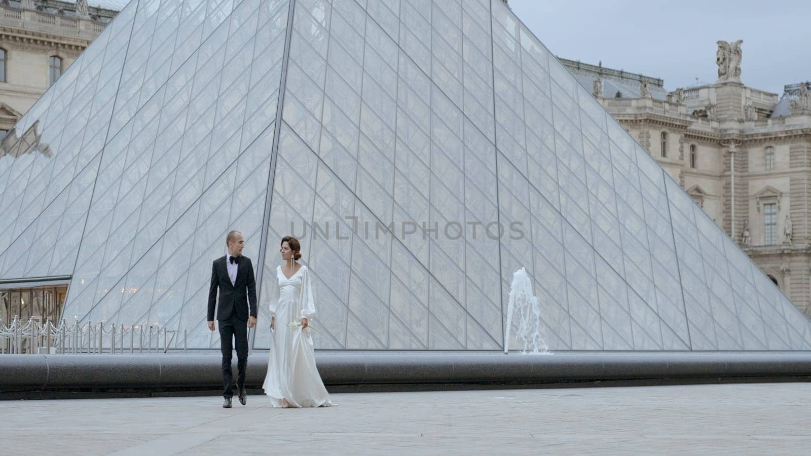 Wedding couple walking on the background of the Louvre pyramid, France, Paris. Action. Romantic wedding shooting near museum