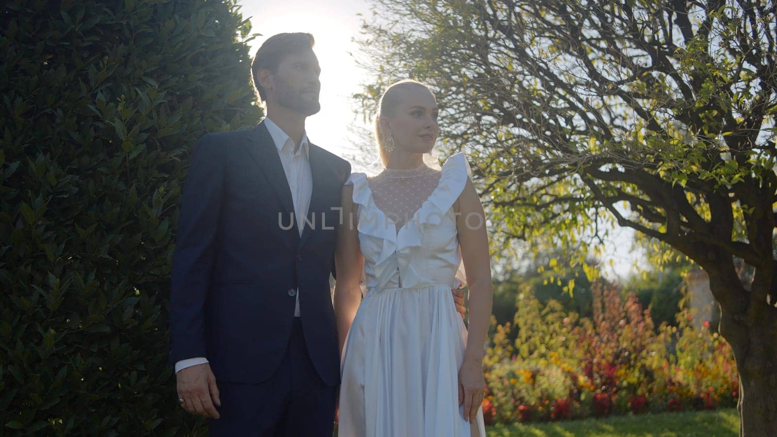 Bride and groom walking in the park. Action. A beautiful landscape with a green park where elegant newlyweds are walking by the hand. High quality 4k footage