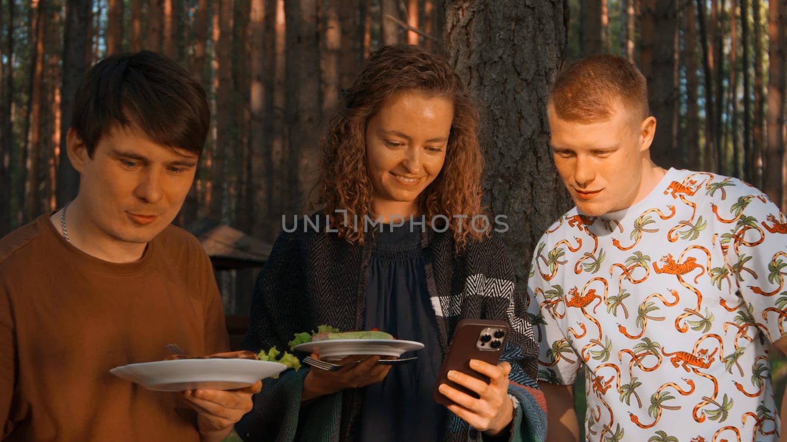 Group of friends eating barbecue and laughing fun by the grill. Stock footage. Girl showing something funny in her smartphone