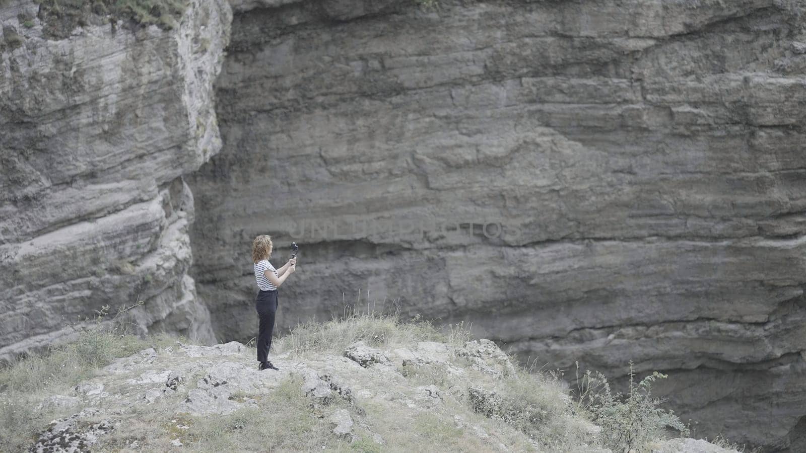 Woman takes pictures on phone with steadicam of mountain. Action. Beautiful woman in the mountains among rocks takes pictures on phone. Woman professionally shoots rock landscapes and waterfalls on phone.