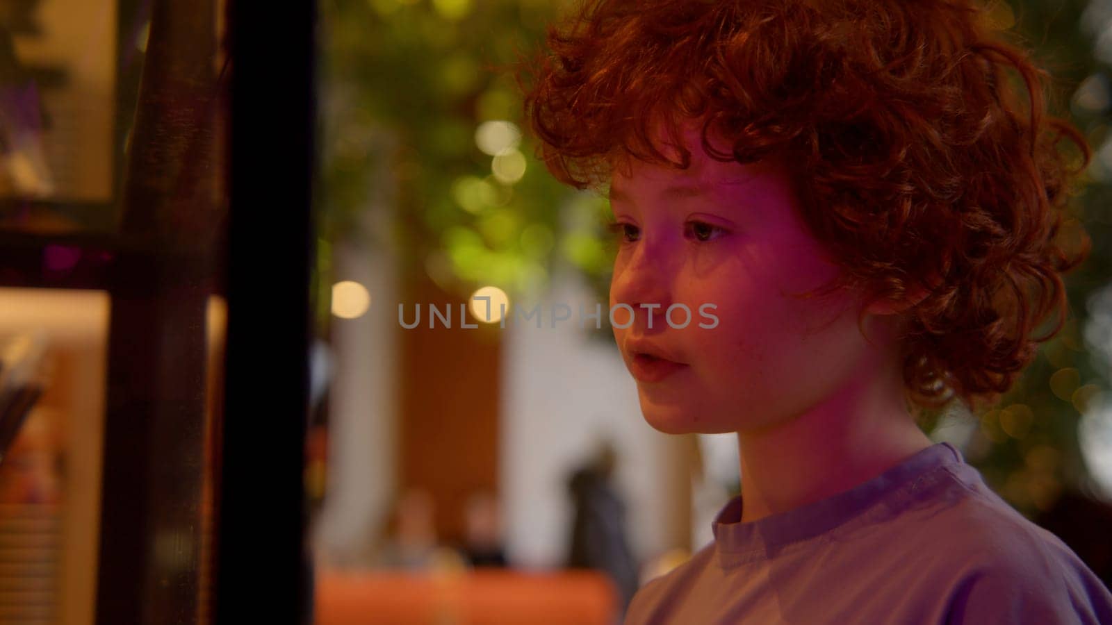 Red haired cute boy on the background of the interior with green leaves. Stock footage. Curly hair of a little boy