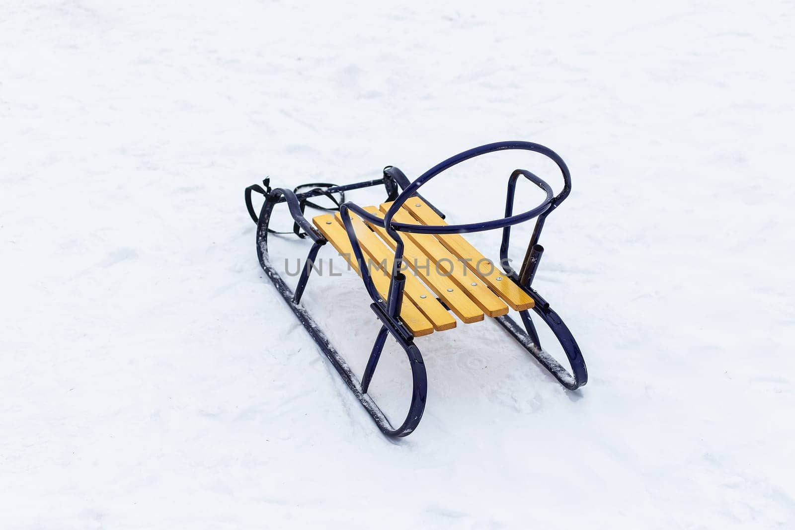 Wooden sleigh with blue metal frame and yellow seat on snowy surface, showing children's winter and outdoor games