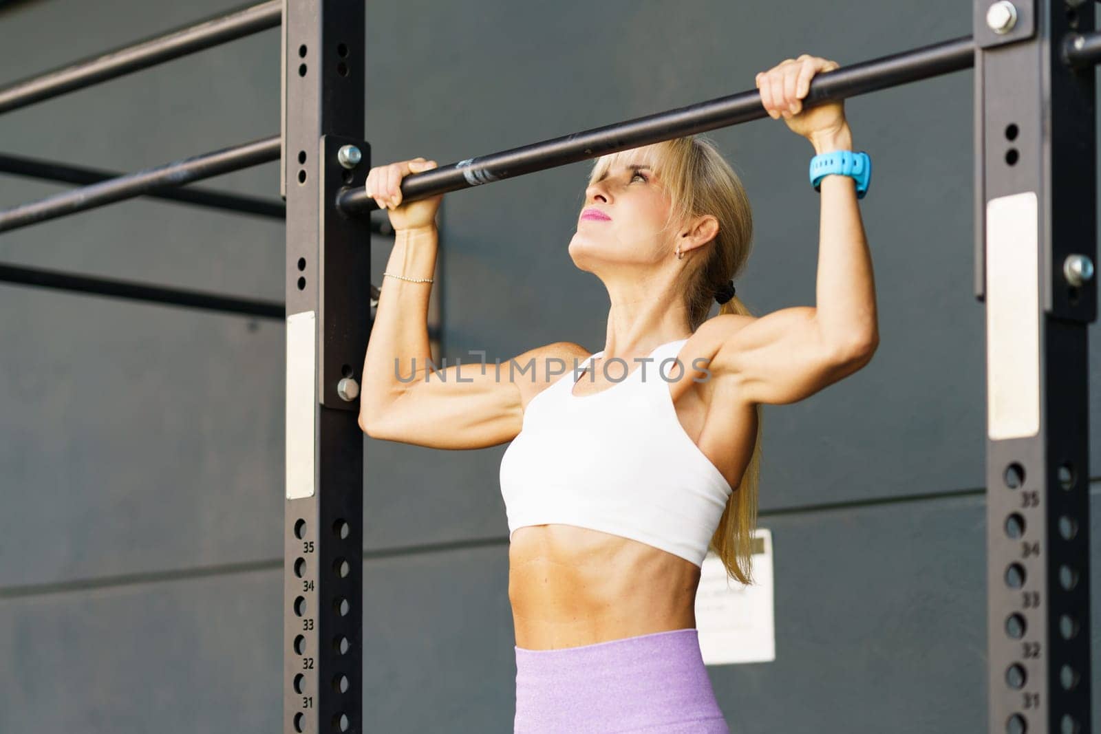 Strong young woman hanging on bar in gym by javiindy