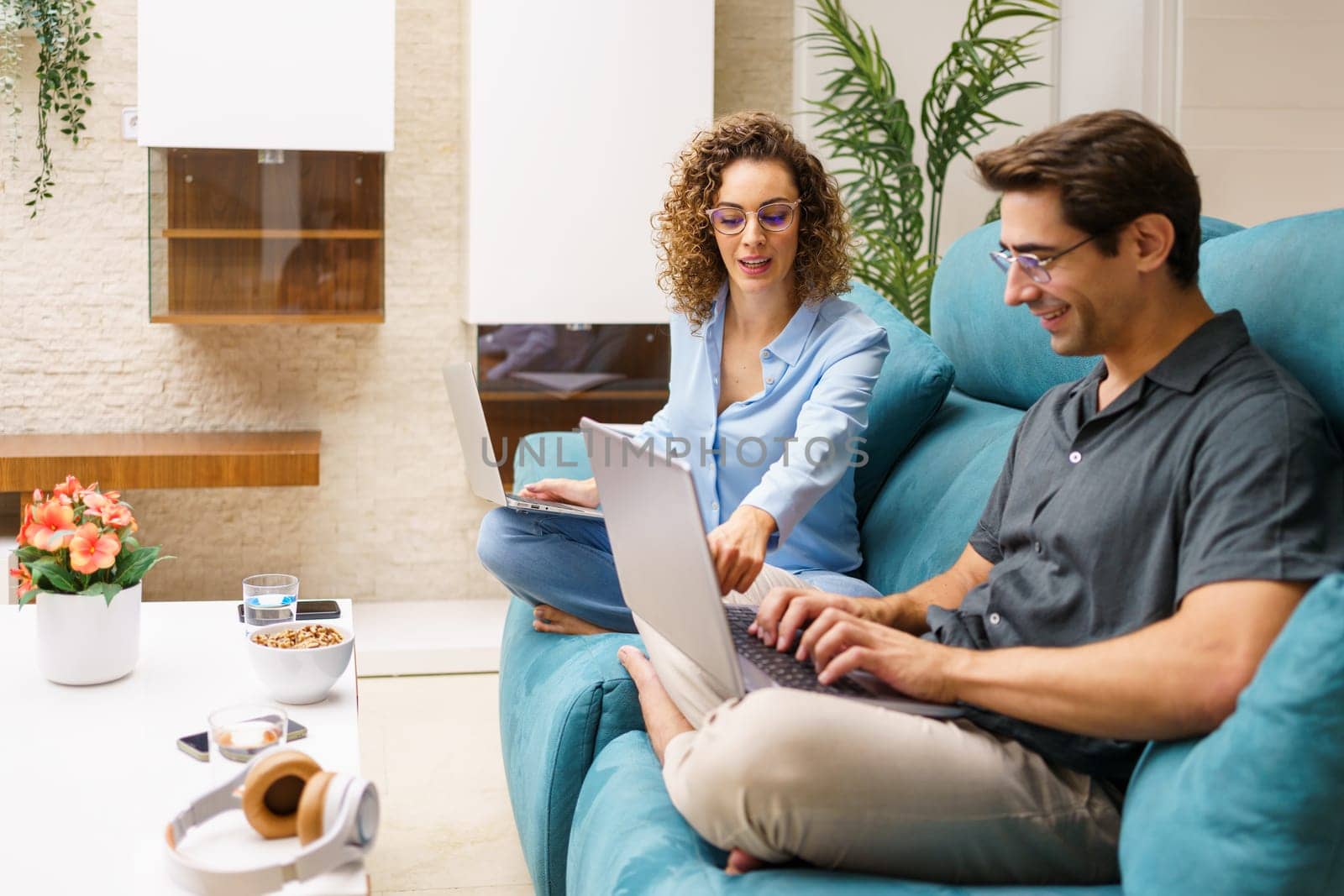 Cheerful couple working on laptop while looking at screen in living room by javiindy