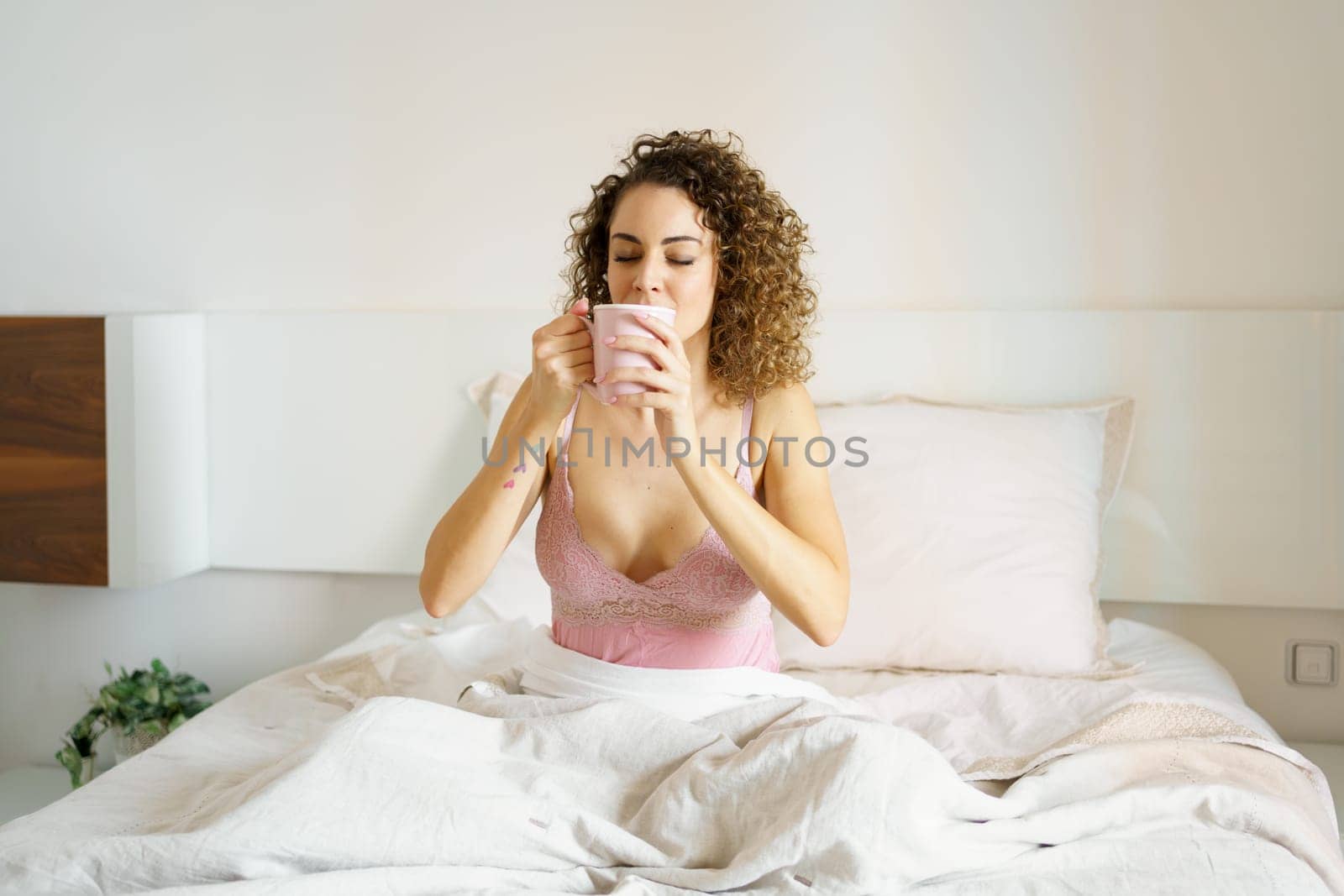 Woman in nightwear drinking fresh coffee in bed by javiindy