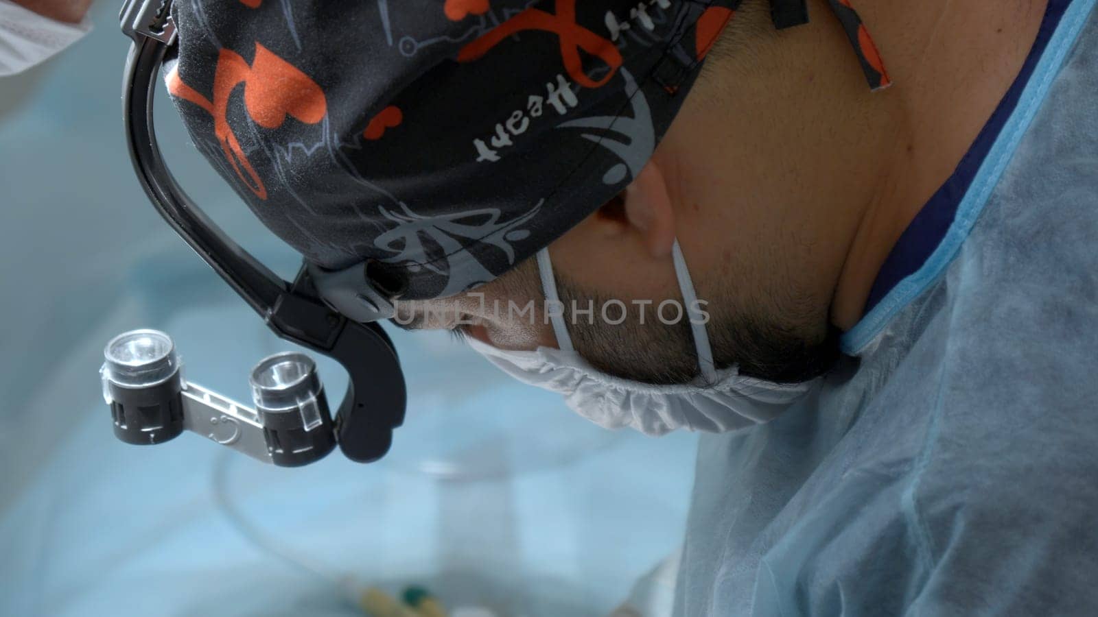 A close up male medical worker with a disposable mask and hat is wearing a special equipment on his head. Action. Surgeon at work in modern clinic