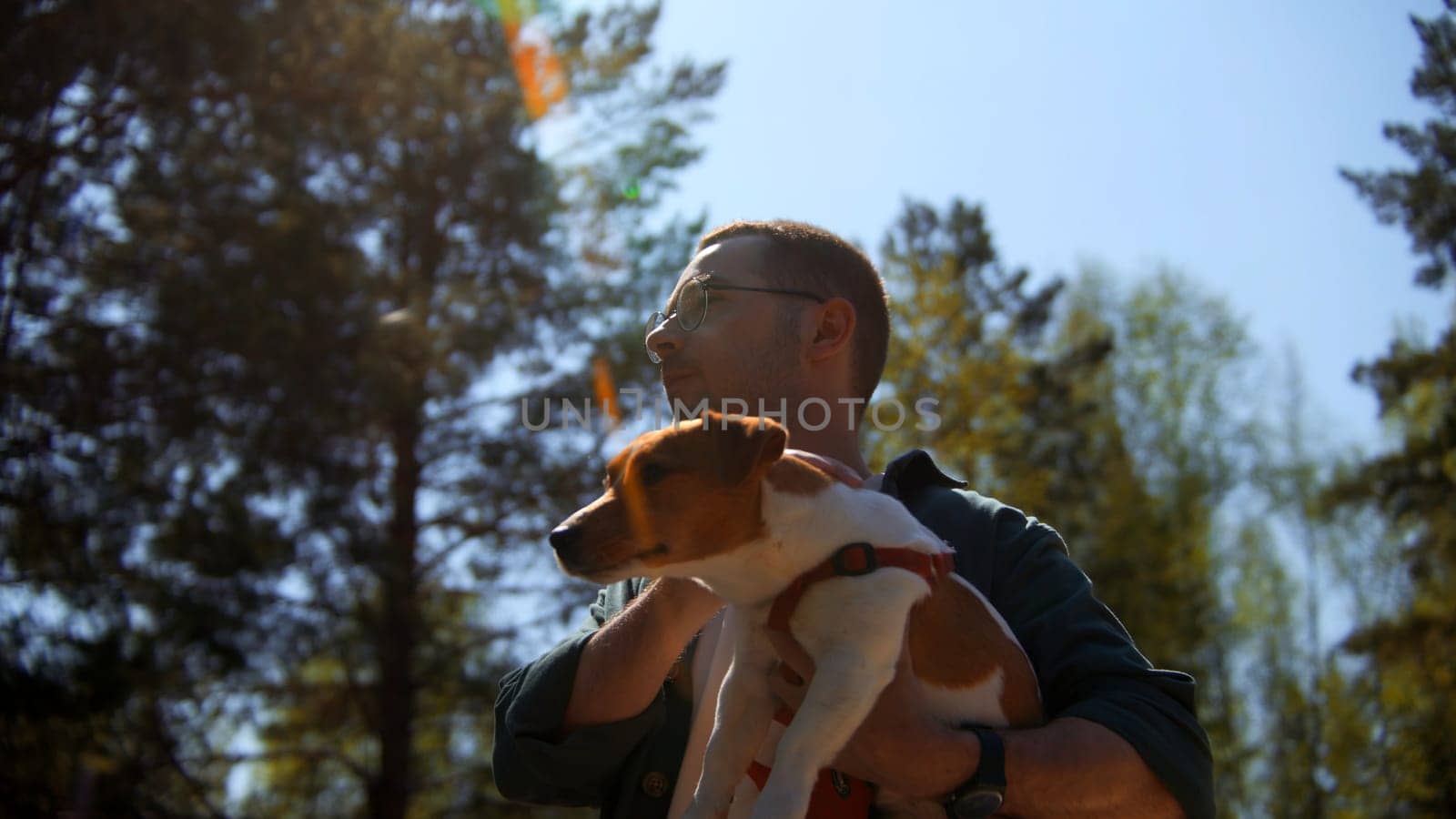 Positive young man holding his beloved dog Jack Russell Terrier and is enjoying a sunny summer day. Stock footage. The concept of love for pets