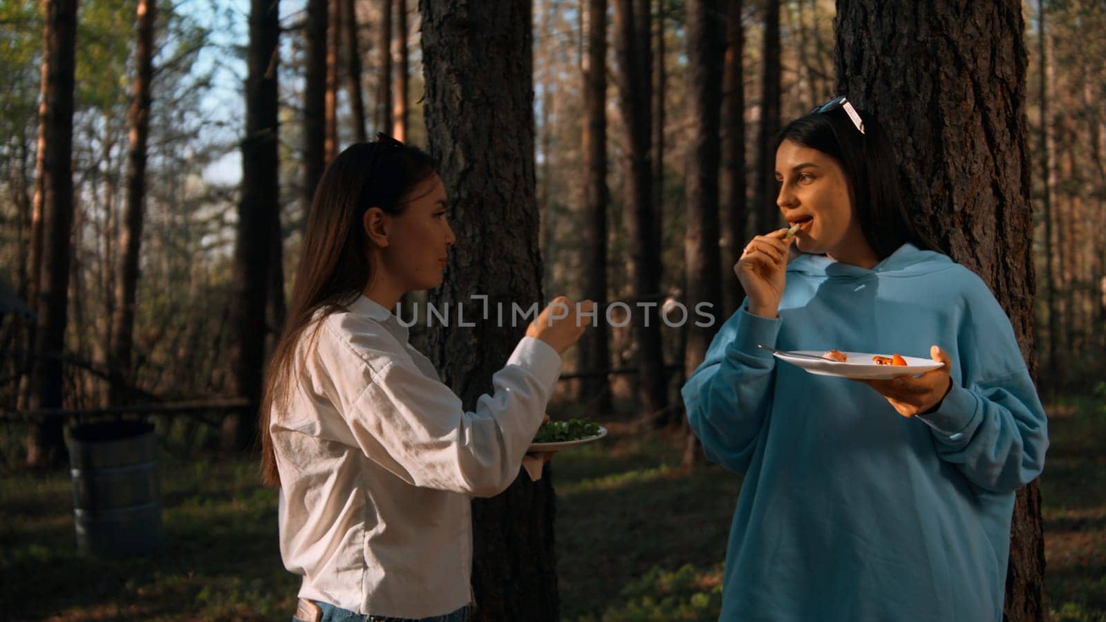 Barbecue on a summer day in coniferous forest. Stock footage. Two adult girls standing and communicating while eating