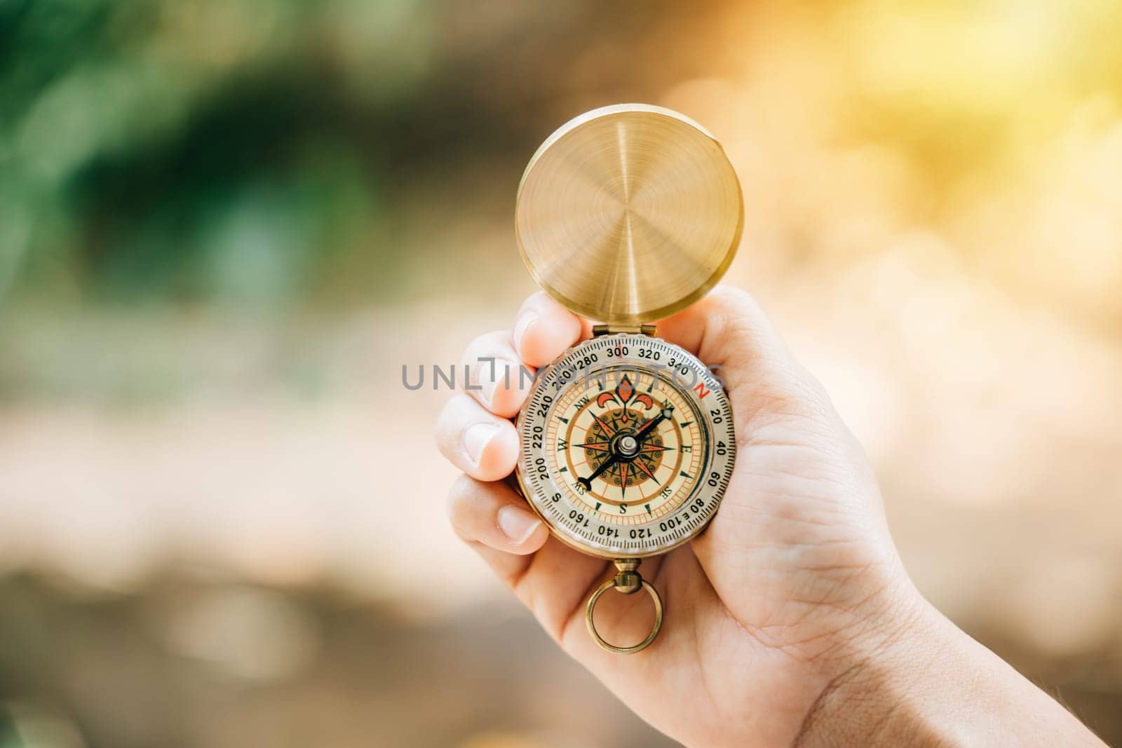 Discover your path in nature with a hand holding a compass amidst the green forest. This image offers copy space for text and embodies travel lifestyle and successful business management. by Sorapop