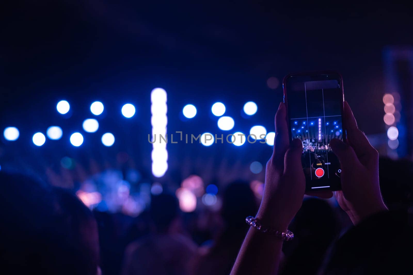 An electrifying concert festival during main event as cheering unrecognizable crowd gathers in front of brightly lit stage at night. lens flare adds to fun capturing excitement of music festival.