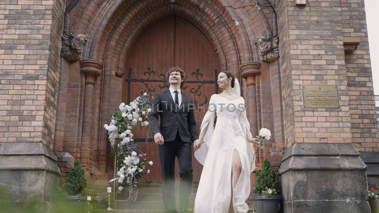 Happy newlyweds leave church. Action. Wedding and newlyweds in old church. Beautiful newlyweds walk from Church to wedding ceremony.