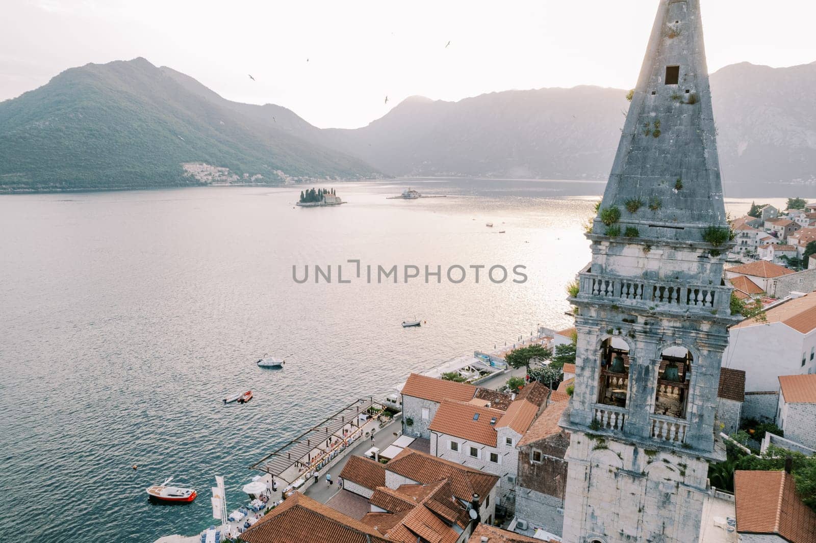 Bell tower of the Church of St. Nicholas among ancient houses against the backdrop of the islands of the Bay of Kotor. Perast, Montenegro. High quality photo