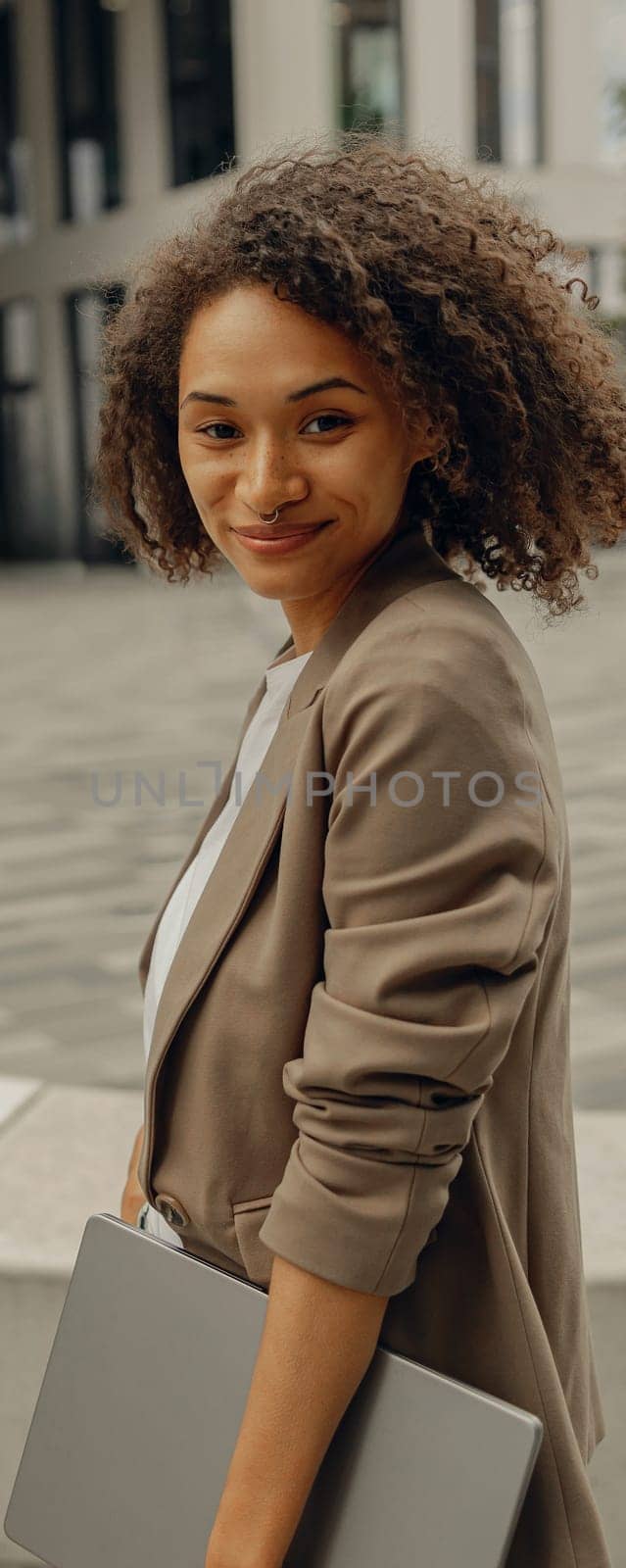 Smiling businesswoman standing with laptop on office building background during break time