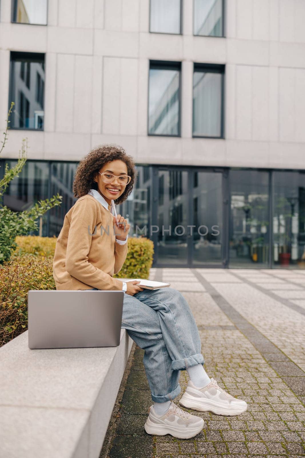 Smiling business woman working laptop and making notes sitting on background of office building by Yaroslav_astakhov
