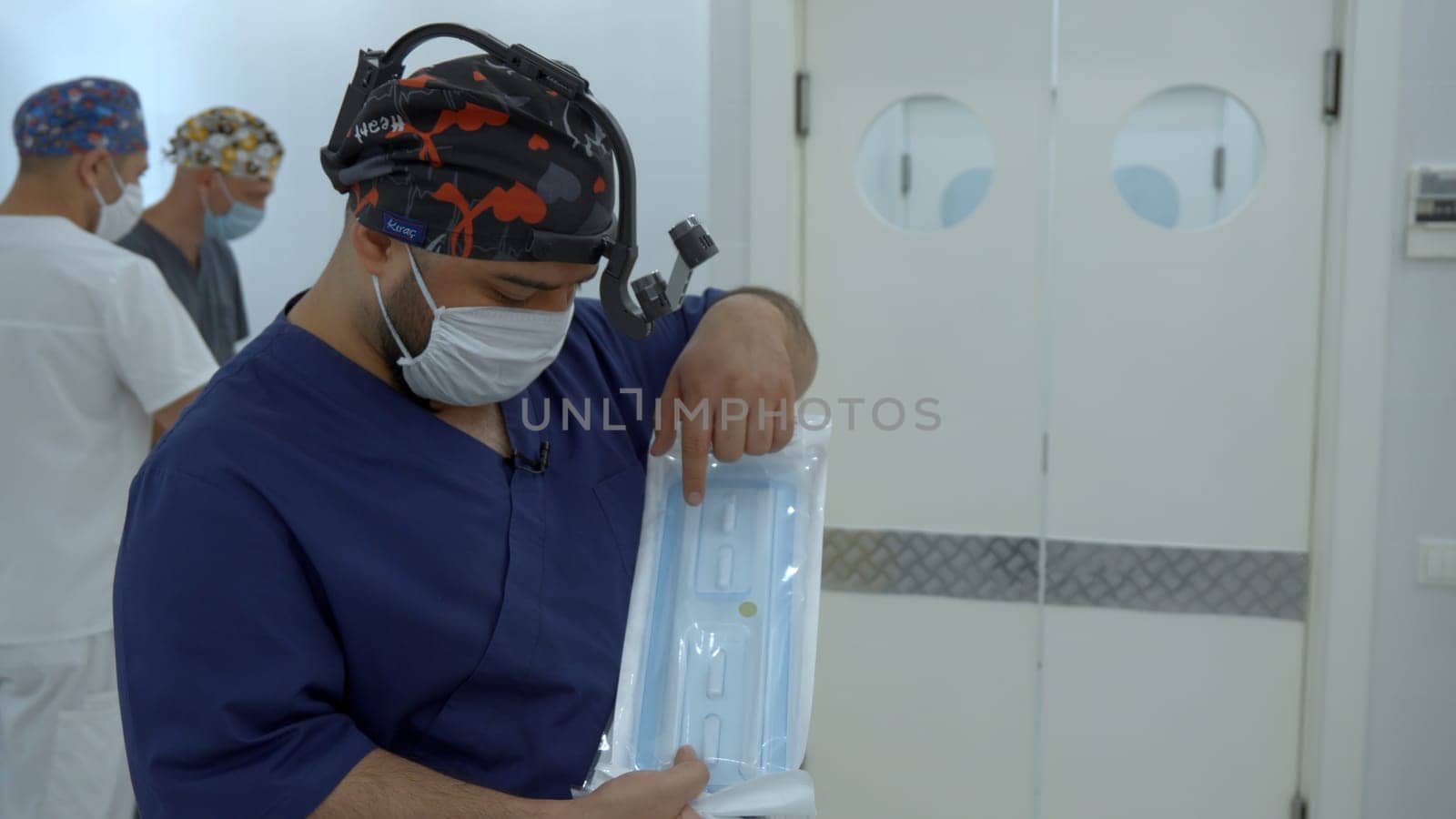 Male caucasian otolaryngologist portrait in surgery room. Action. Doctor showing sterile equipment