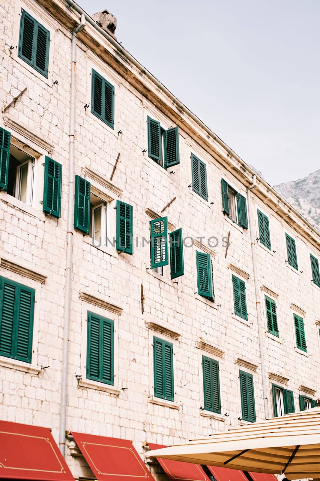 Stone facade of an ancient apartment building with green shutters on the windows by Nadtochiy