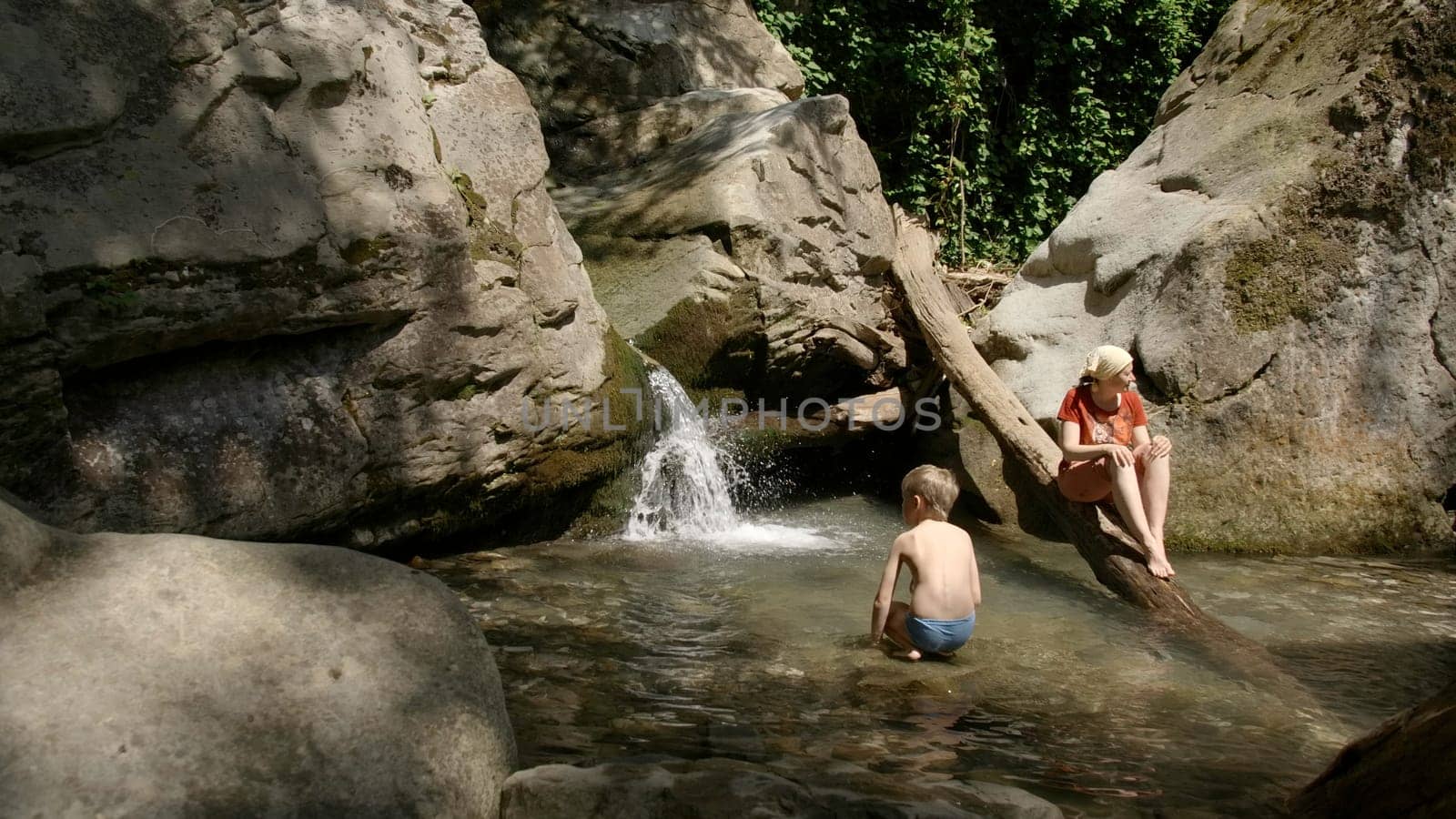A mother and her son swimming in a mountain creek in northern Sweden. Creative. Concept of summer vacation, cold water stream among rocks. by Mediawhalestock