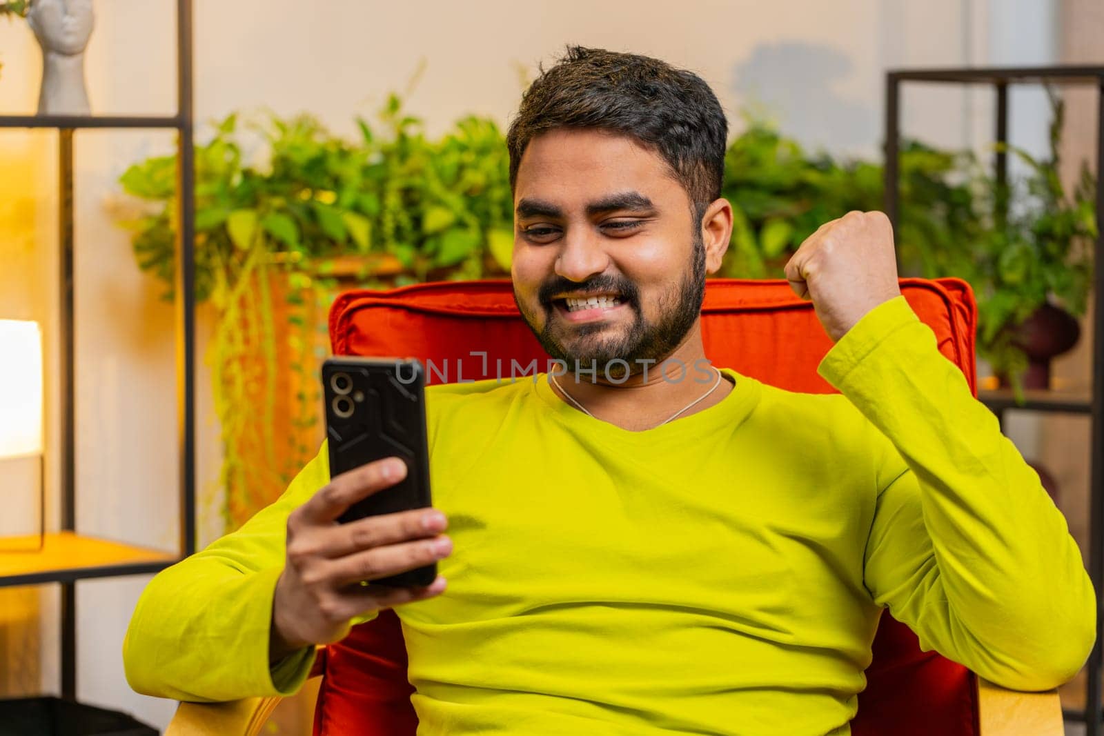 Happy man use mobile smartphone typing browsing say Wow yes, celebrating success victory, winning lottery jackpot goal achievement play games, good positive news, triumph. Guy at home in room on chair