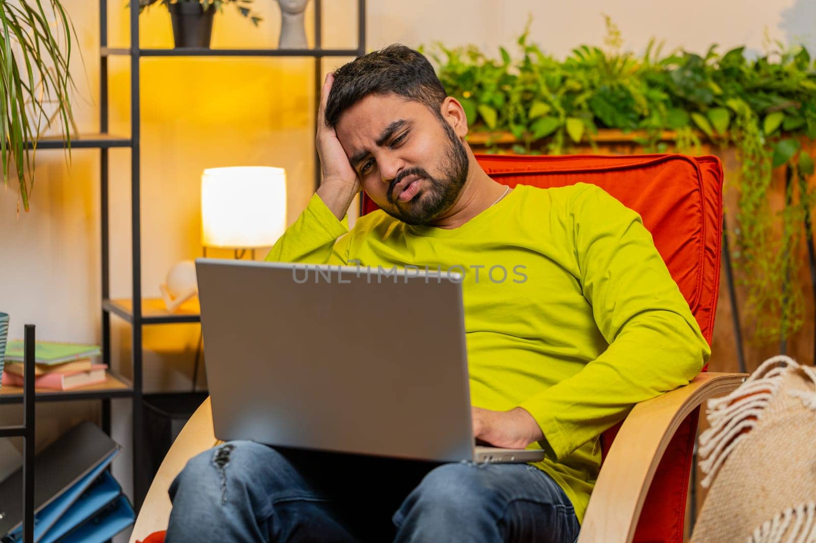 Displeased sad Indian Arab man use laptop notebook typing browsing working, loses becoming surprised sudden lottery results bad news fortune loss game fail computer virus. Arabian guy at home on chair