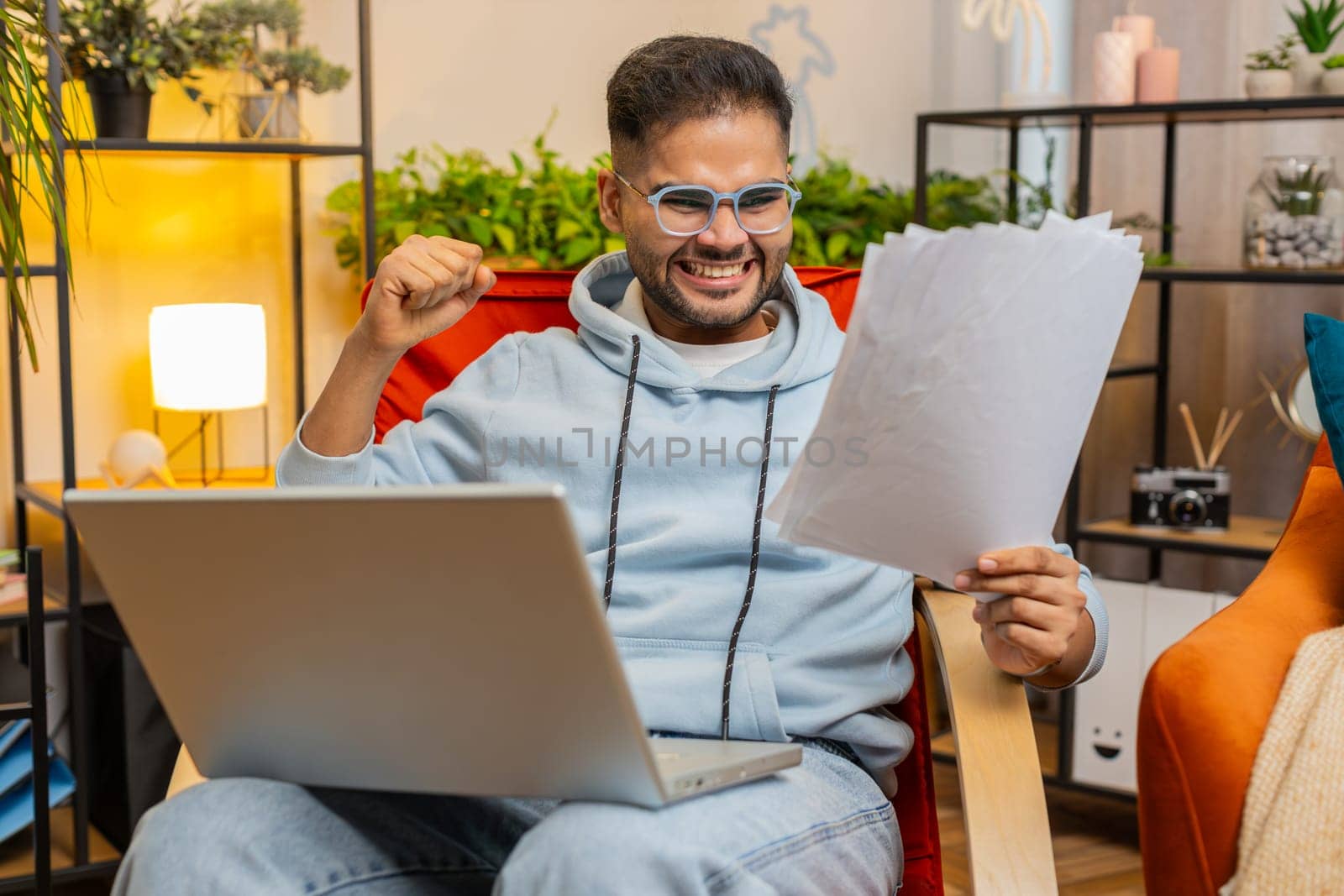 Stressed Indian man working on laptop at home room looking at unpaid bank debt bills doing paperwork planning budget calculate finances mortgage payments. Angry displeased guy scream on paper bills