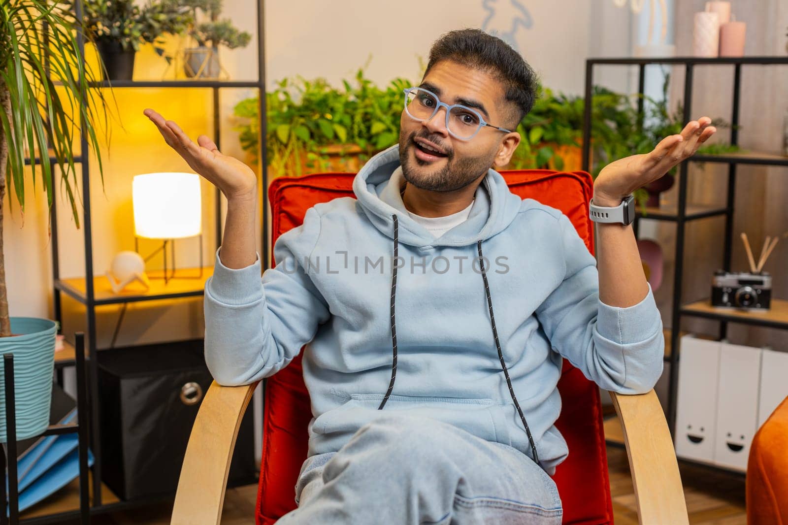 What. Why. Frustrated Indian man raising hands in indignant expression, asking reason of failure, demonstrating disbelief irritation by troubles, quarrel at home room apartment. Guy sits on chair