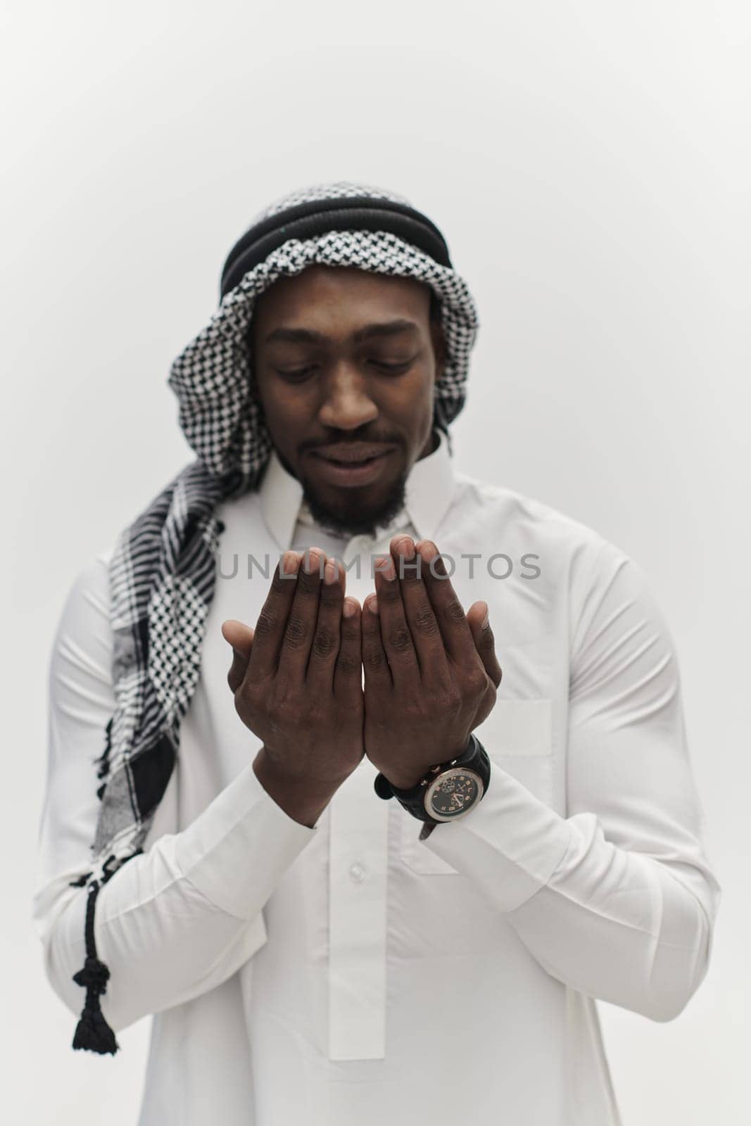 African American Muslim man raises his hands in prayer, seeking solace and devotion to God, as he stands isolated against a serene white backdrop, symbolizing a profound expression of faith and contemplation by dotshock