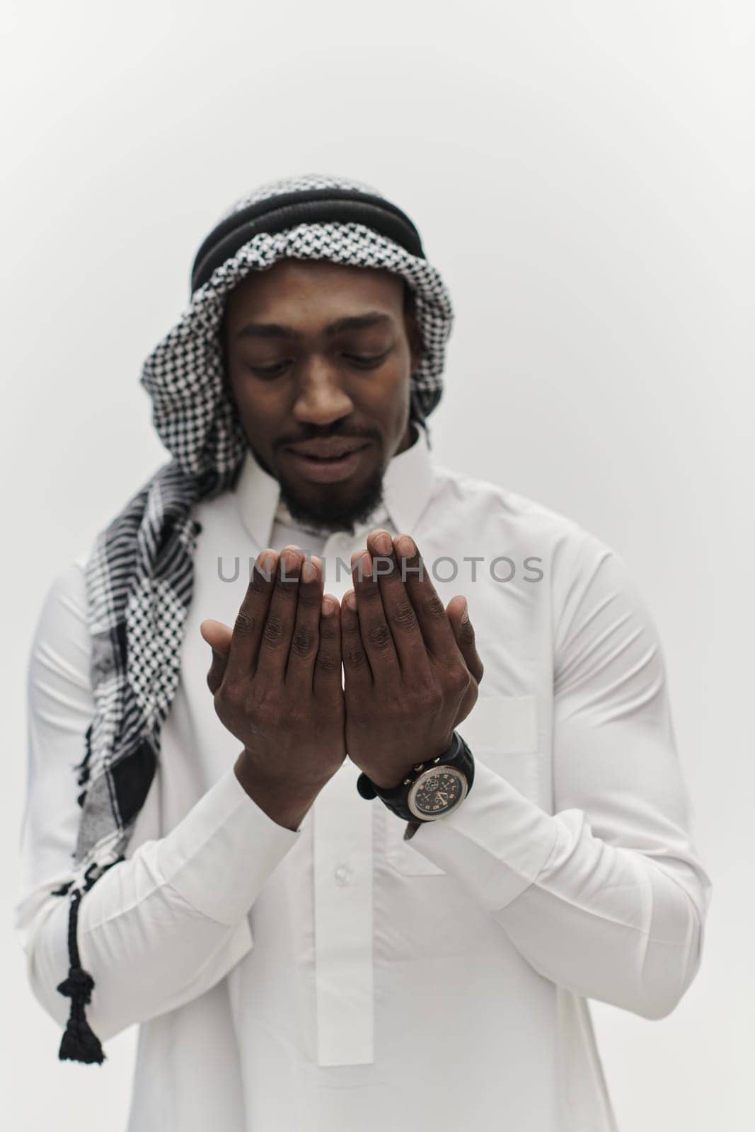 African American Muslim man raises his hands in prayer, seeking solace and devotion to God, as he stands isolated against a serene white backdrop, symbolizing a profound expression of faith and contemplation.