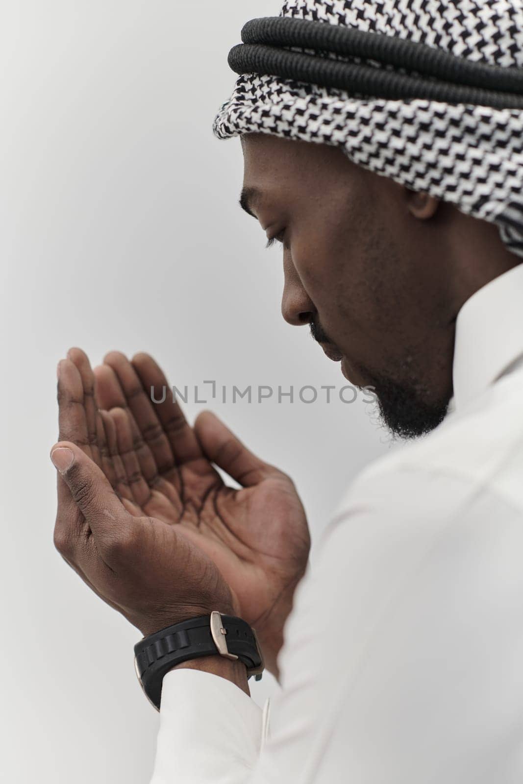 African American Muslim man raises his hands in prayer, seeking solace and devotion to God, as he stands isolated against a serene white backdrop, symbolizing a profound expression of faith and contemplation by dotshock