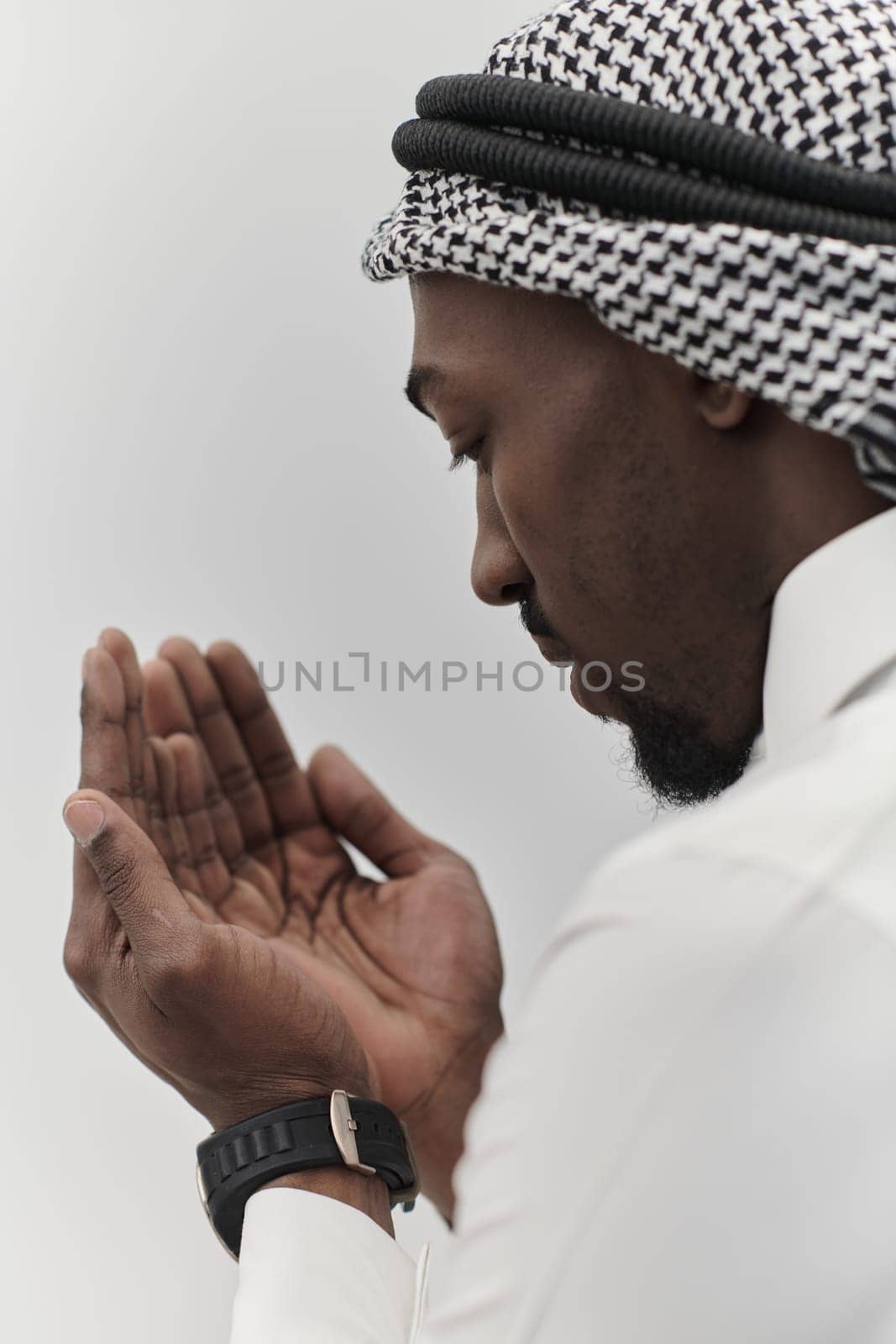 African American Muslim man raises his hands in prayer, seeking solace and devotion to God, as he stands isolated against a serene white backdrop, symbolizing a profound expression of faith and contemplation.