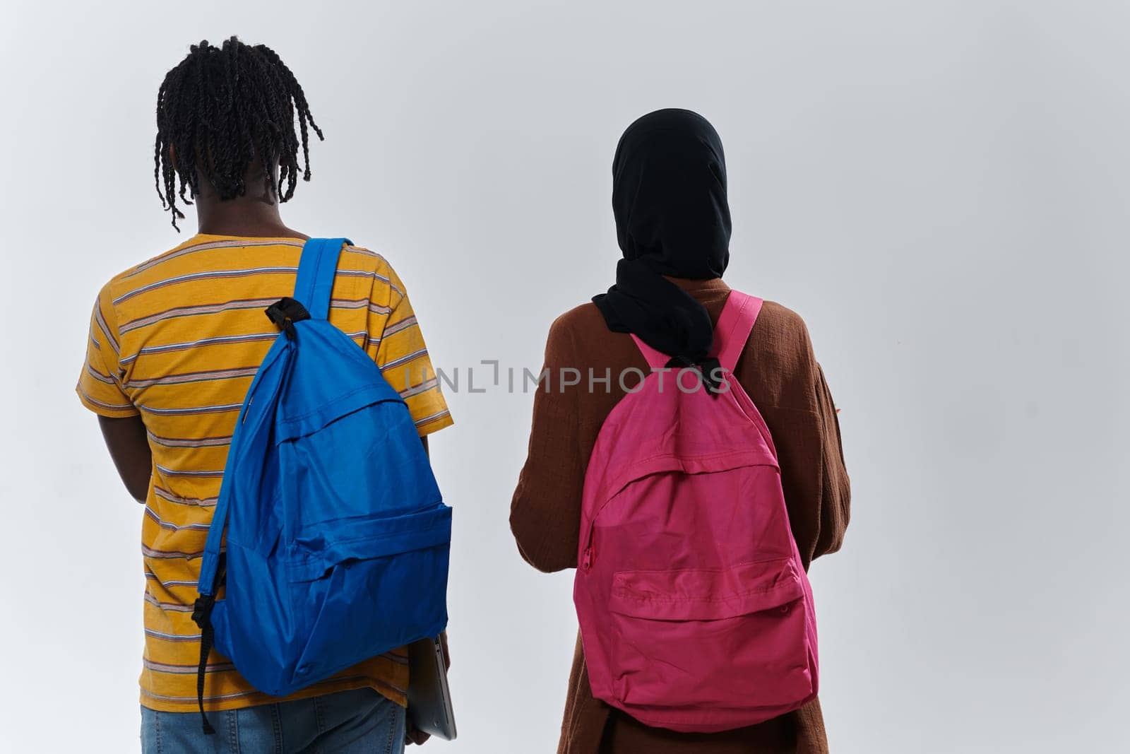 African American student collaborates with his Muslim colleague, who diligently works on her laptop, symbolizing a blend of diversity, modern learning, and cooperative spirit against a serene white background.