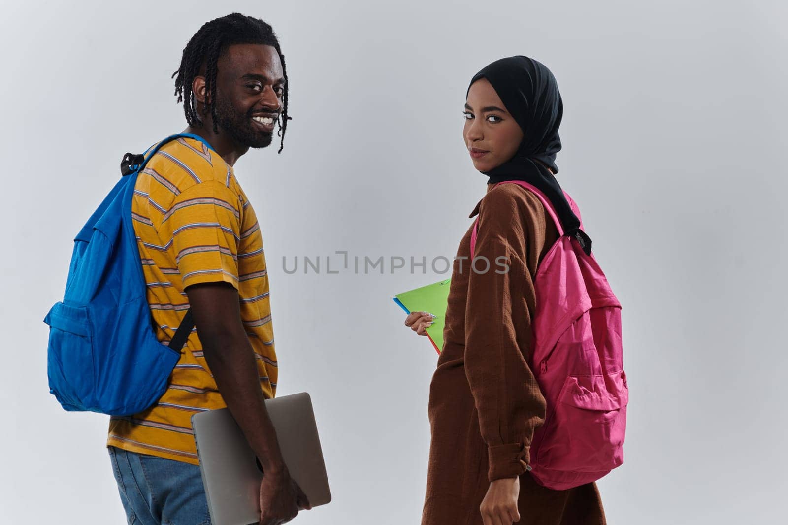 African American student collaborates with his Muslim colleague, who diligently works on her laptop, symbolizing a blend of diversity, modern learning, and cooperative spirit against a serene white background.